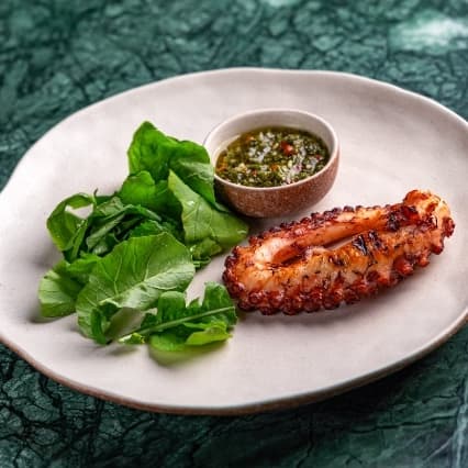 Octopus — Grilled octopus with a smoky finish and tender texture. Served with fresh greens and flavorful dress