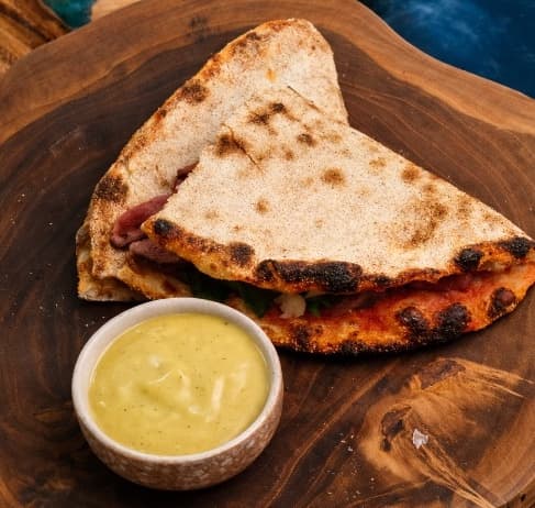 Roastbeef sandwich — Crispy pizza-dough flatbread filled with roast beef, parmesan, rucola, and capers. Served with cream