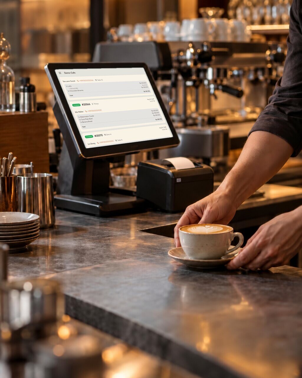 A POS terminal on the bar counter, a barista placing a cappuccino